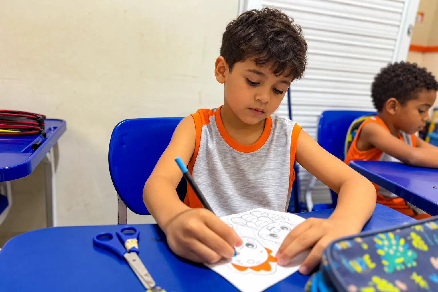 Aluno do IEST colorindo um desenho na carteira da sala de aula